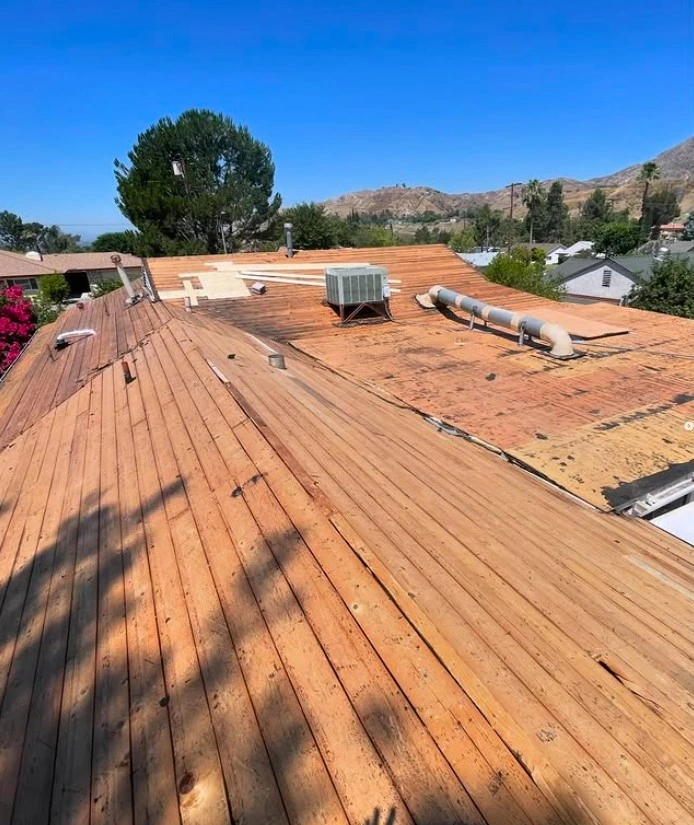 Exposed wooden roof decking during roof replacement on a residential home under clear blue skies.